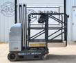 JLG vertical mast lift, silver power unit, black guardrails around the platform, mast lowered, four wheels