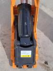 Hydraulic cylinder mounted between the orange side plates with a caution add-oil-before-use label below