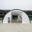 White fabric building with green trim, front door open on a concrete pad