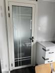 Frosted-glass bathroom door in white aluminum frame with black lever handle, kitchenette cabinet beside it