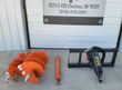 Post hole digger kit: orange auger bits and an extension beside the black drive unit on its quick-attach frame