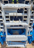Folded gray scissor-arm stack and perforated steel access ladder on the blue chassis, lift fully lowered