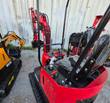 Operator seat, joystick levers and rubber track of a red Miva VA13 mini excavator, with other mini excavators nearby