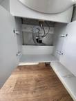 Open vanity cabinet under the sink: gray P-trap drain, flexible supply lines and empty storage shelf