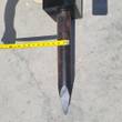Pointed moil bit of the hydraulic breaker with a tape measure across the shank, about 2 inches wide