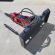 Red Raytree hydraulic breaker on a skid steer quick-attach plate, hoses coiled, spare chisel bit alongside