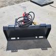 Skid steer power rake attachment: red hydraulic valve block and coiled hoses on a toothed-edge frame