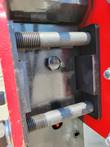 Post driver's pivot pin and mounting bolt, close-up of the red bracket hinge