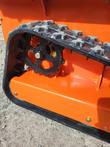 Rubber track and black drive sprocket on the orange tracked mower body, close-up