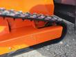 Orange track frame with access plate and rubber track, idler end, flail mower undercarriage close-up