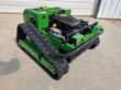 Green tracked remote control mower, front three-quarter view: RATO engine, red emergency stop, rubber tracks and black bumper