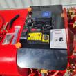 Yellow remote control, 20V battery, charger and manual on the black deck of the sprayer, nozzle ring at right