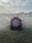 Red tracked orchard sprayer from the rear, caged axial fan and tracks, spray mist drifting over a grass field