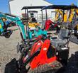Red mini skid steer on rubber tracks with canopy, seat, hydraulic hoses and bucket, other mini machines behind