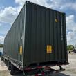 Dark green high-cube shipping container loaded on a flatbed trailer, corrugated steel sides