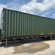 Full-length green shipping container on a flatbed trailer, cargo doors at the near end, ribbed steel side