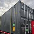 Charcoal gray high-cube shipping container, closed cargo doors with four steel lock rods, strapped to a flatbed