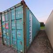 Weathered teal used shipping container, rust at the corner posts, closed cargo doors with steel lock rods