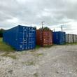 Row of shipping containers: long blue unit in front, rust red and shorter blue beside it, weathered gray units behind