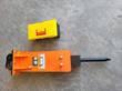 Orange hydraulic excavator breaker, black mounting plate and chisel, laid flat next to a yellow toolbox for scale
