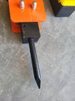 Black chisel and tool holder block under the orange mount plate of a hydraulic breaker, acorn nuts on top, toolbox beside