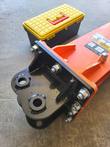 Black mounting bracket with two pin bores and bolts on the top of an orange hydraulic breaker, yellow toolbox behind