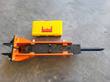 Orange hydraulic breaker with side cover open, showing the black hydraulic cylinder block with IN and OUT ports