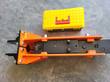 Orange hydraulic breaker from above: black cylinder block with IN and OUT ports, mount plate, toolbox above, chisel cut off