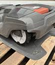 Husqvarna robotic mower on its docking base, side view with gray body and red-orange hatch