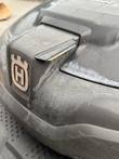 Husqvarna logo on the front cover of a robotic mower, with light scuffing on the gray plastic