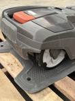 Husqvarna robotic mower on its charging station, side view of the drive wheel and red-orange top cover