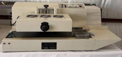 Cream continuous induction cap sealer, front view: conveyor, sealing head with three fans and nameplate