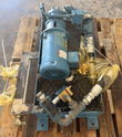 Blue hydraulic power unit seen from the motor end, with gear pump, valves and bagged fittings on a pallet