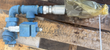 Blue pipe elbow and tee with a hydraulic hose fitting and brass block lying on wood pallet slats