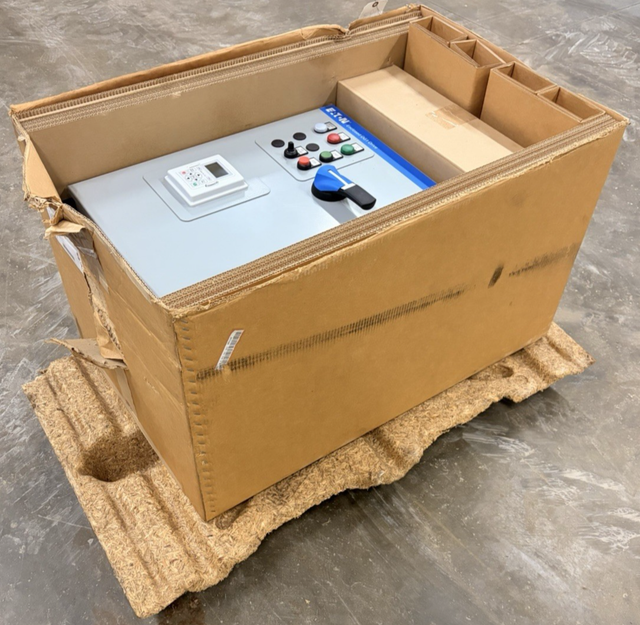 Eaton Enclosed DG1 drive cabinet packed in a torn cardboard box on a pallet, door facing up