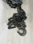 Pile of load chain ending in a latched hook, with the hoist body cut off at the top of the frame