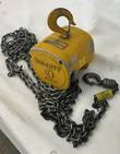Yellow Budgit 1 ton manual chain hoist with top hook, load chain and bottom hook on a white surface