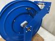 Blue spring-driven hose reel at an angle, hub with gray swivel mount and guide arm
