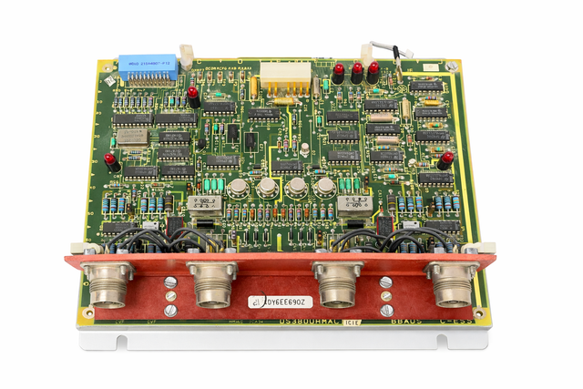 Top view of a GE circuit board with ICs, red LEDs, blue connector and four round connectors on white