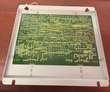 Underside of a circuit board in a gray metal mounting tray, showing solder traces