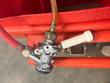 Chrome keg coupler with red gas hose and clear beer line on the red cart