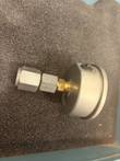 Back of a pressure gauge with brass fitting and steel hex adapter marked 1102 on gray foam