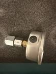 Side of a pressure gauge with brass fitting and steel hex adapter on gray foam