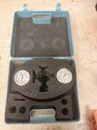 Open blue case with two pressure gauges and cut-out black foam on a work table