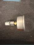 Pressure gauge with brass and steel hex adapter fittings lying beside it on foam