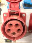 Red round CEE socket with five contact holes and spring-hinged lid on the white box