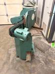 Green double miter saw from the side: motor, mesh belt guard, steel table and foot pedal