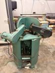 Green dual-head miter saw with two belt-driven blade heads, motors and linkage under the base