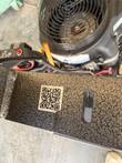 QR code label on the speckled steel frame beside the engine fan guard and control box