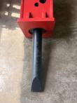 Black chisel tool emerging from the red breaker housing, seen from above